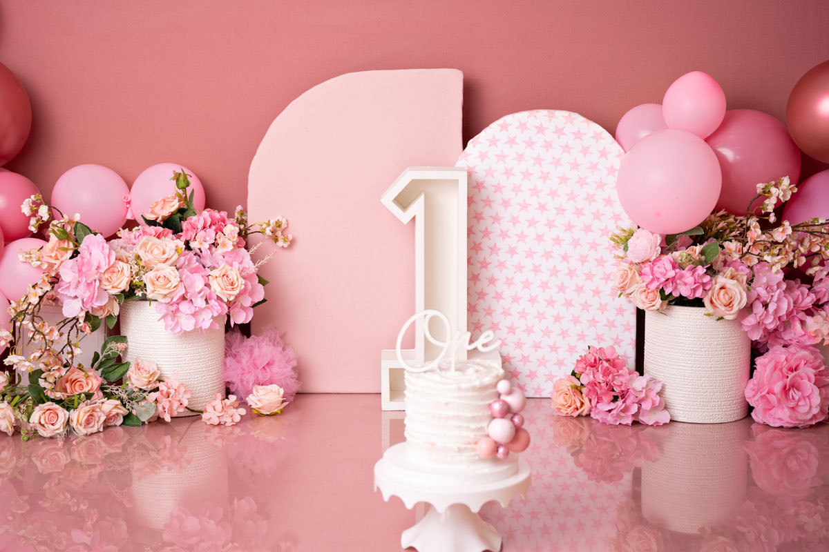 shades of pink cake smash setup with pink backdrop flowers and balloons