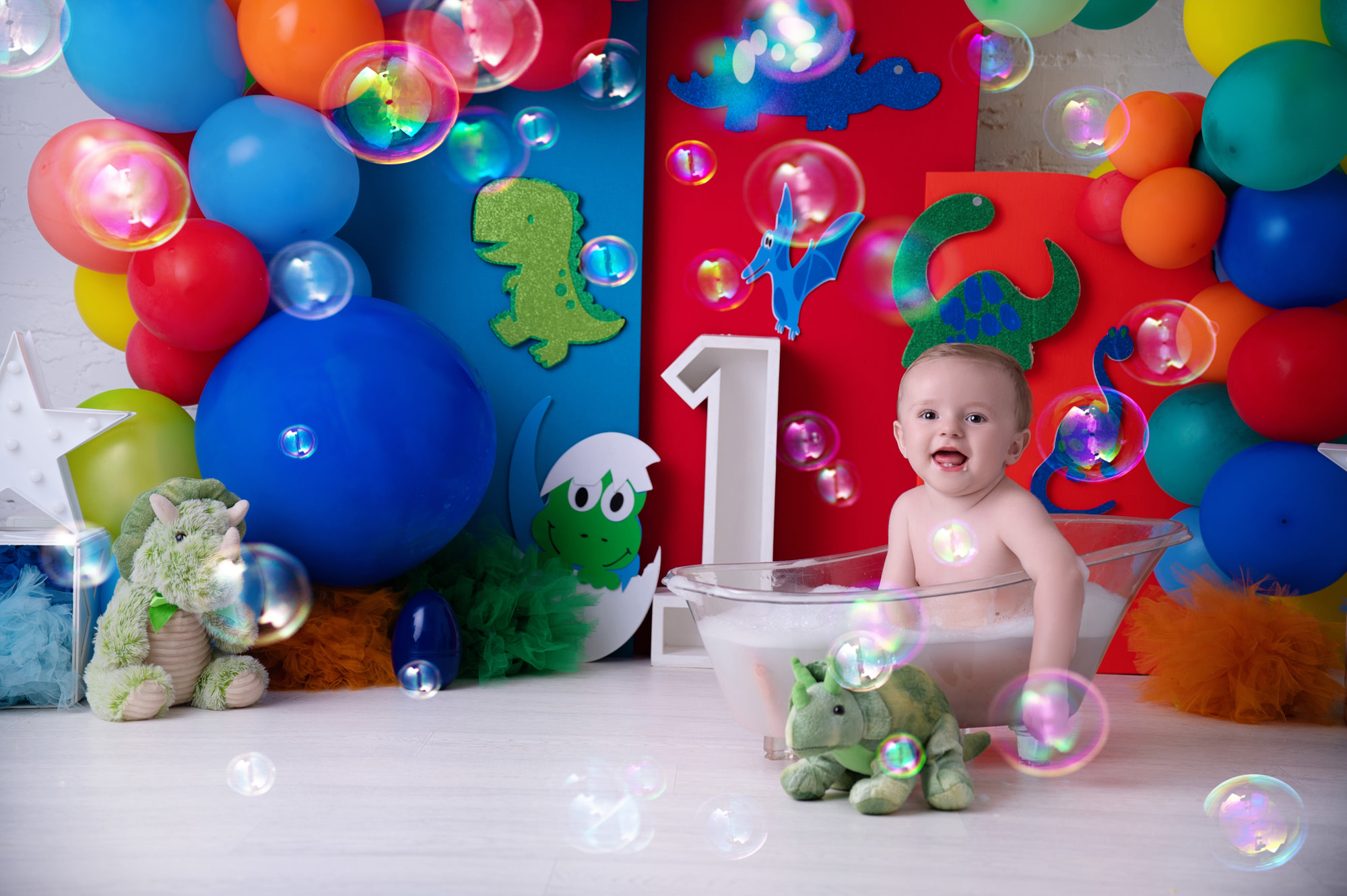 One-year-old sitting in a bubble bath with colourful dinosaur-themed balloons — fun visual for baby swim schools in Pretoria East.