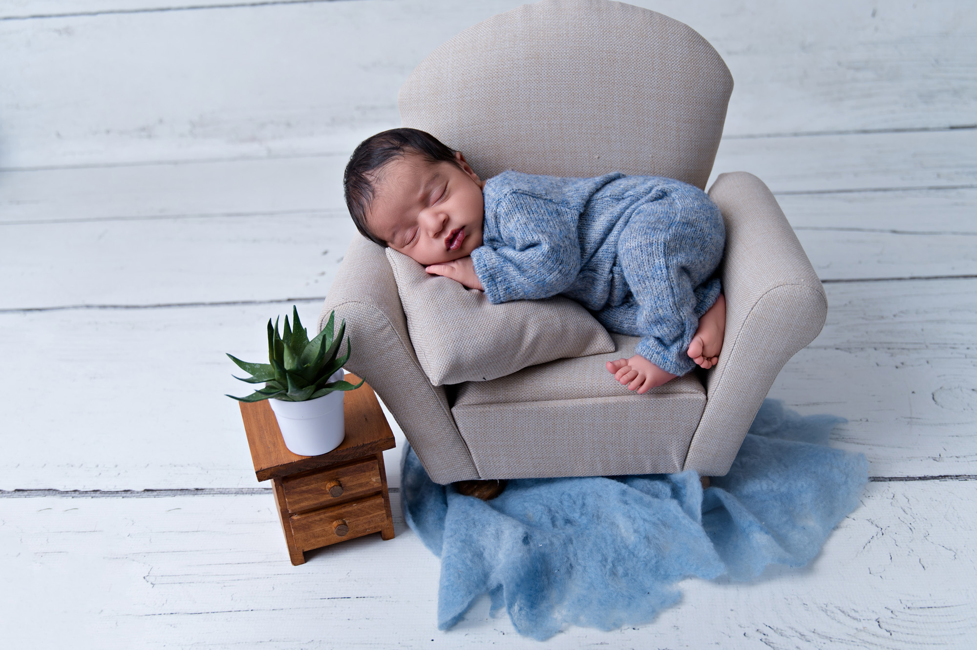 Sleeping newborn baby boy posed on mini armchair with blue textures – newborn photoshoot Pretoria.