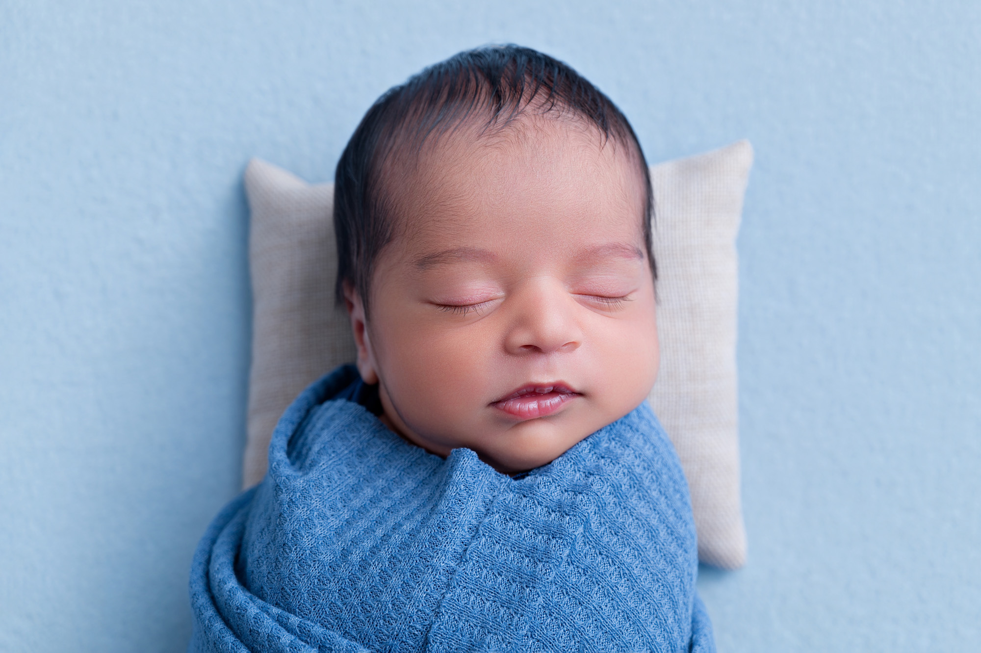 Close-up newborn portrait wrapped in blue blanket with white pillow – Pretoria newborn photographer.
