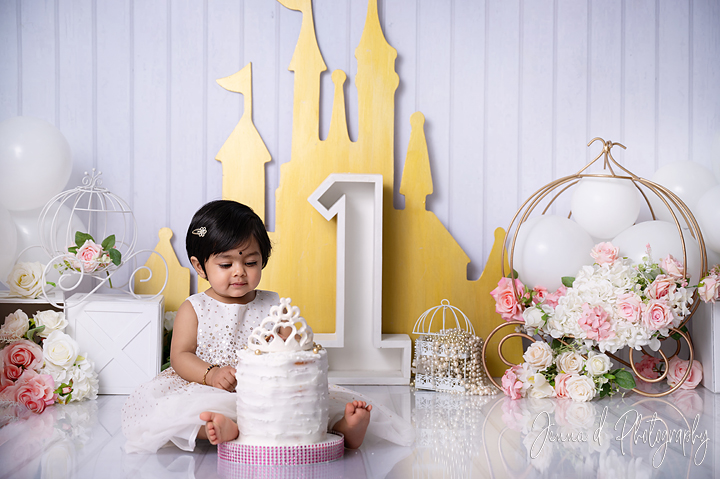 little girl dressed in white eating a white cake with a tiara on the cake