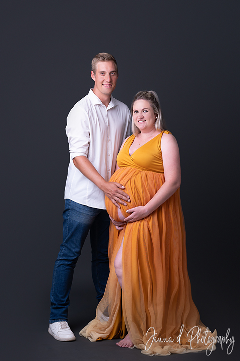 mom and dad in studio grey backdrop wall mustard gold maternity dress