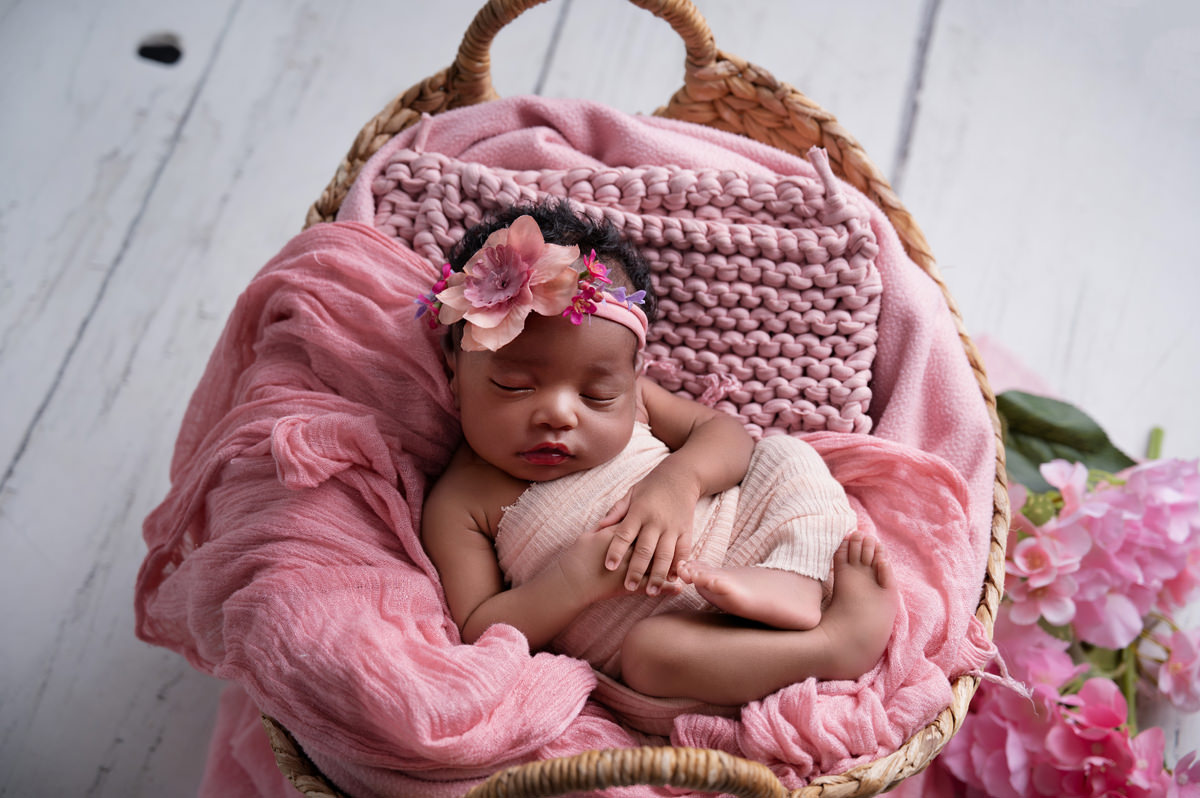 Newborn baby posed in a basket with pink textures, representing the early newborn season when parents look for Baby-Friendly Coffee Shops in Pretoria East.
