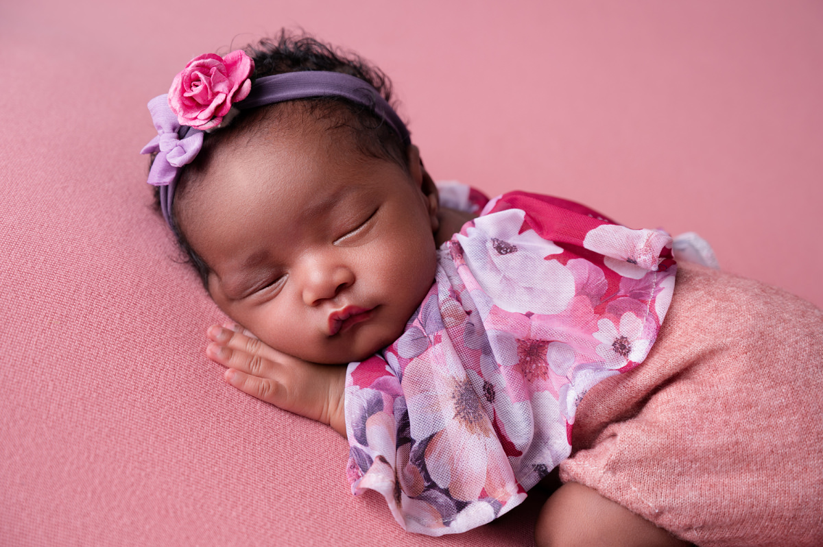 Newborn baby girl sleeping on pink background with floral headband
