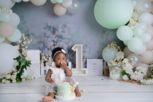 Baby sitting with birthday cake and number one backdrop during 1st Birthday Cake Midstream photoshoot.
