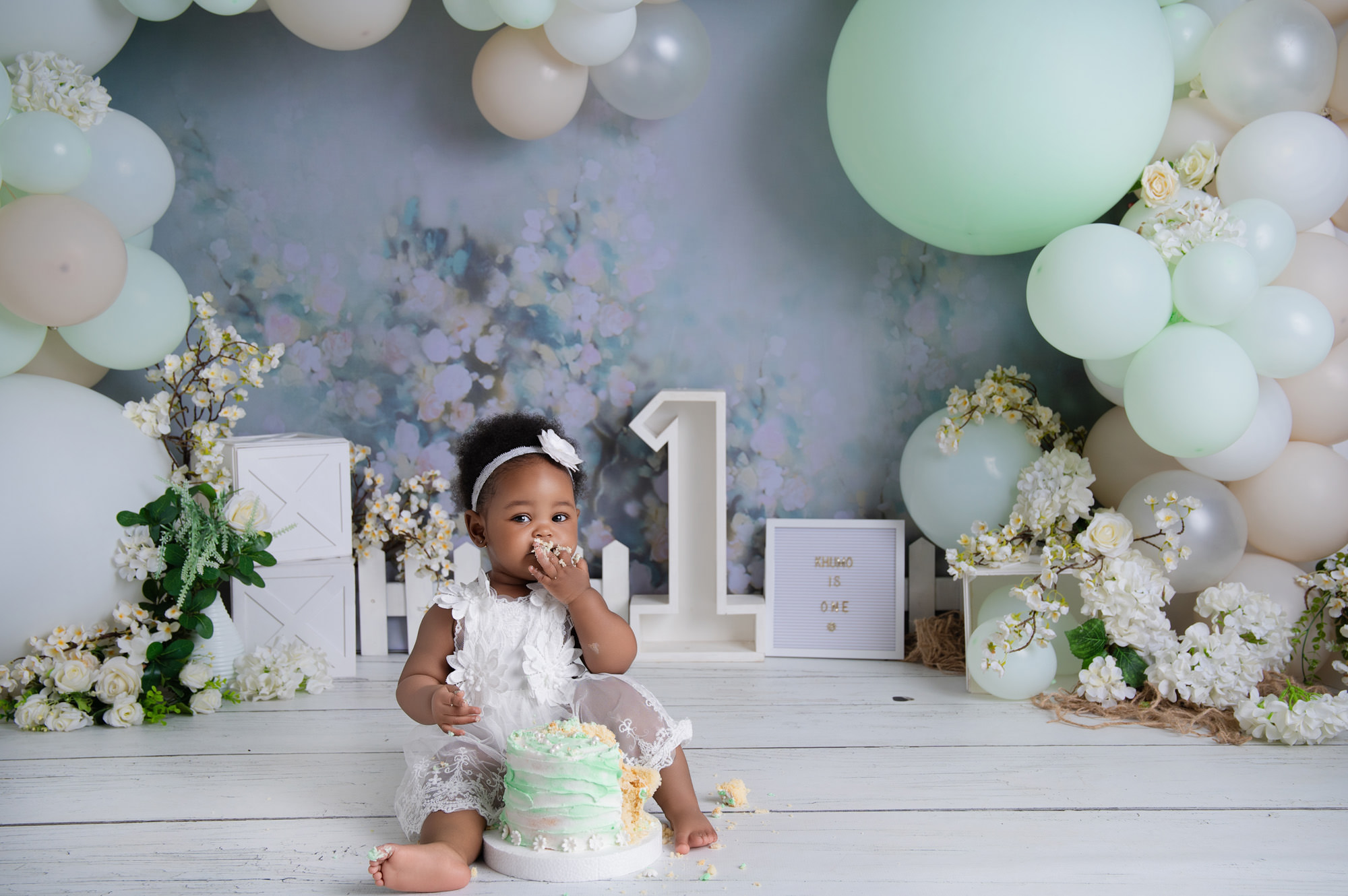 Baby sitting with birthday cake and number one backdrop during 1st Birthday Cake Midstream photoshoot.