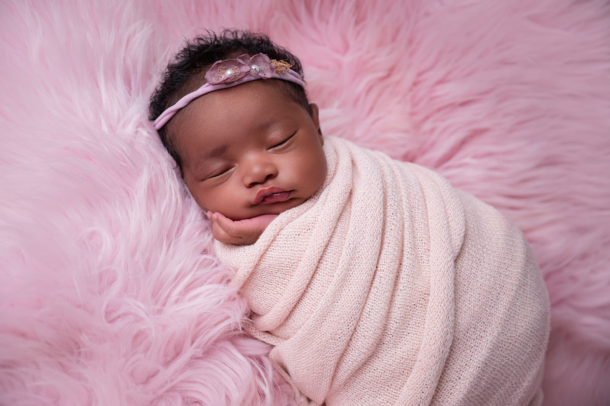 Sleeping newborn baby wrapped in cream on soft pink backdrop during newborn week 1.