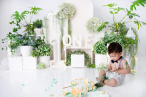 Cake smash moment with baby exploring cake in studio greenery setup – 1st Birthday Cake Bakers in the Moot.