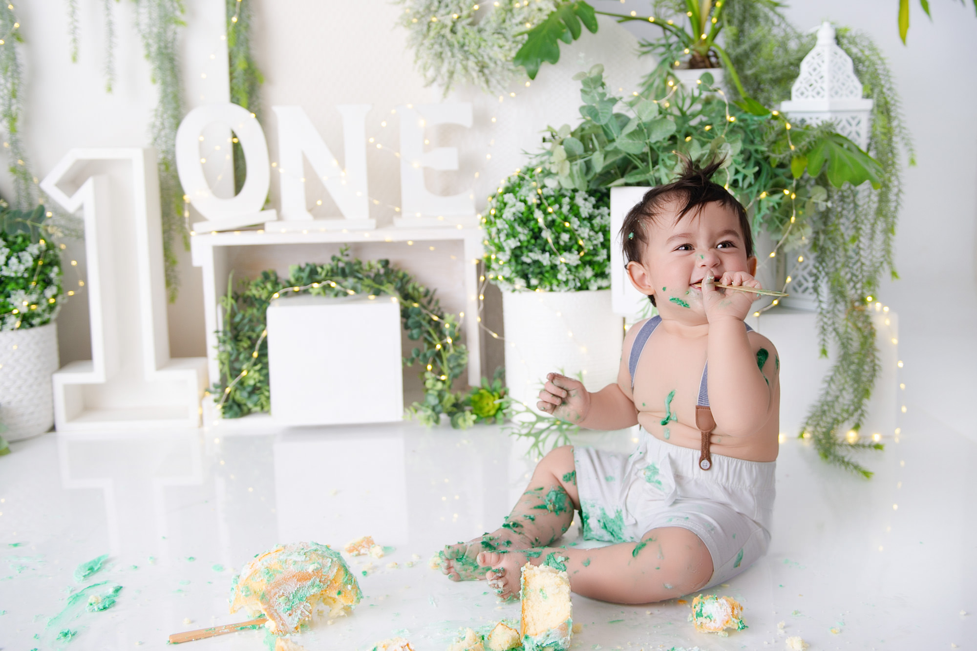 Baby sitting in a greenery “ONE” cake smash setup during 1st Birthday Cake Bakers in the Moot photoshoot.