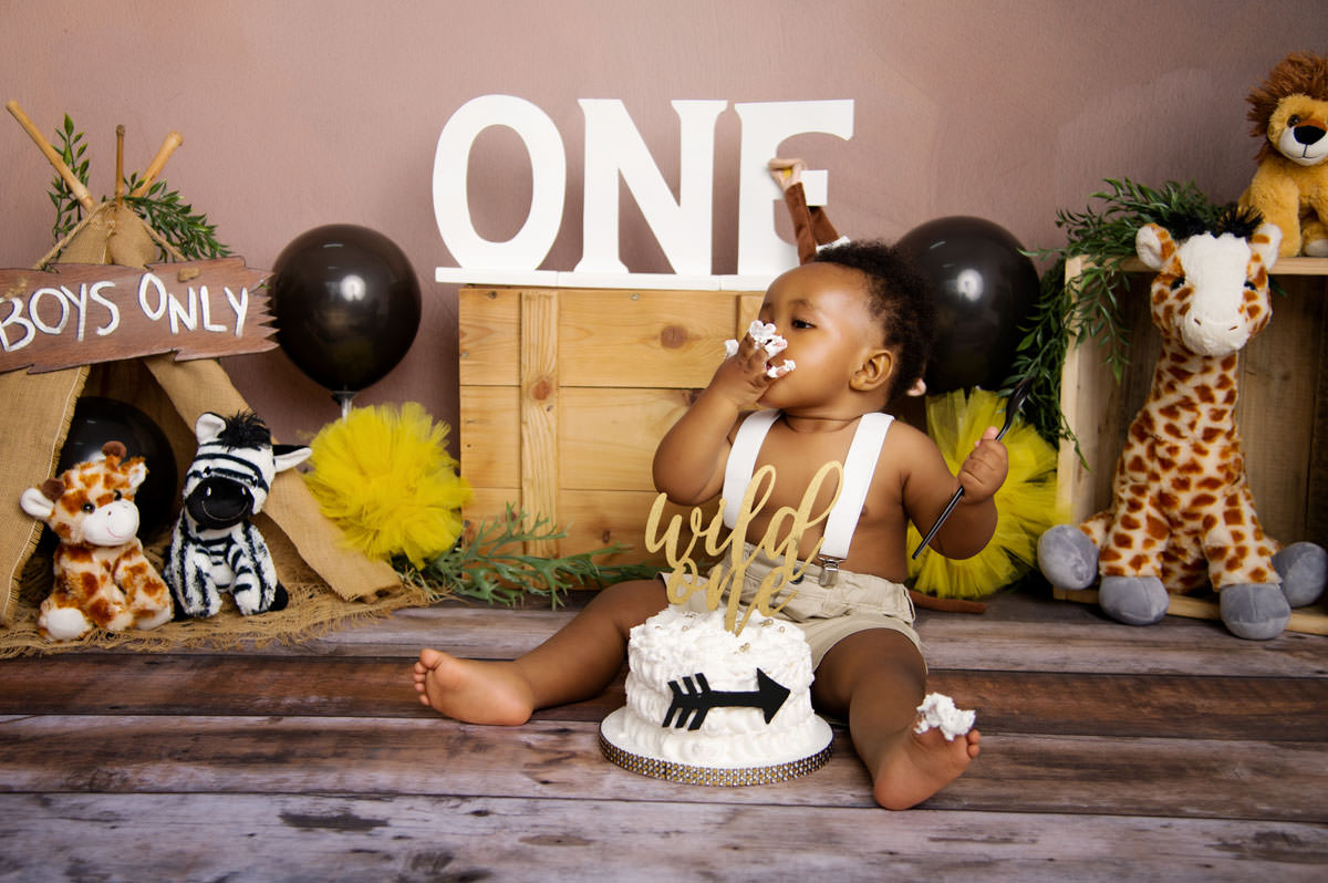 Baby boy sitting next to cake with “ONE” sign backdrop – 1st birthday cake montana cake smash.