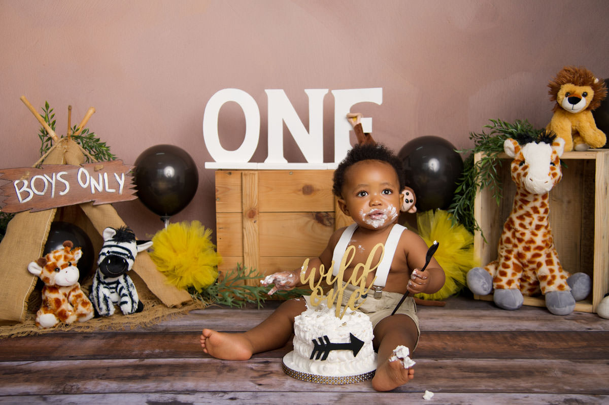 Baby boy sitting with “ONE” backdrop and cake during 1st birthday cake montana photoshoot.