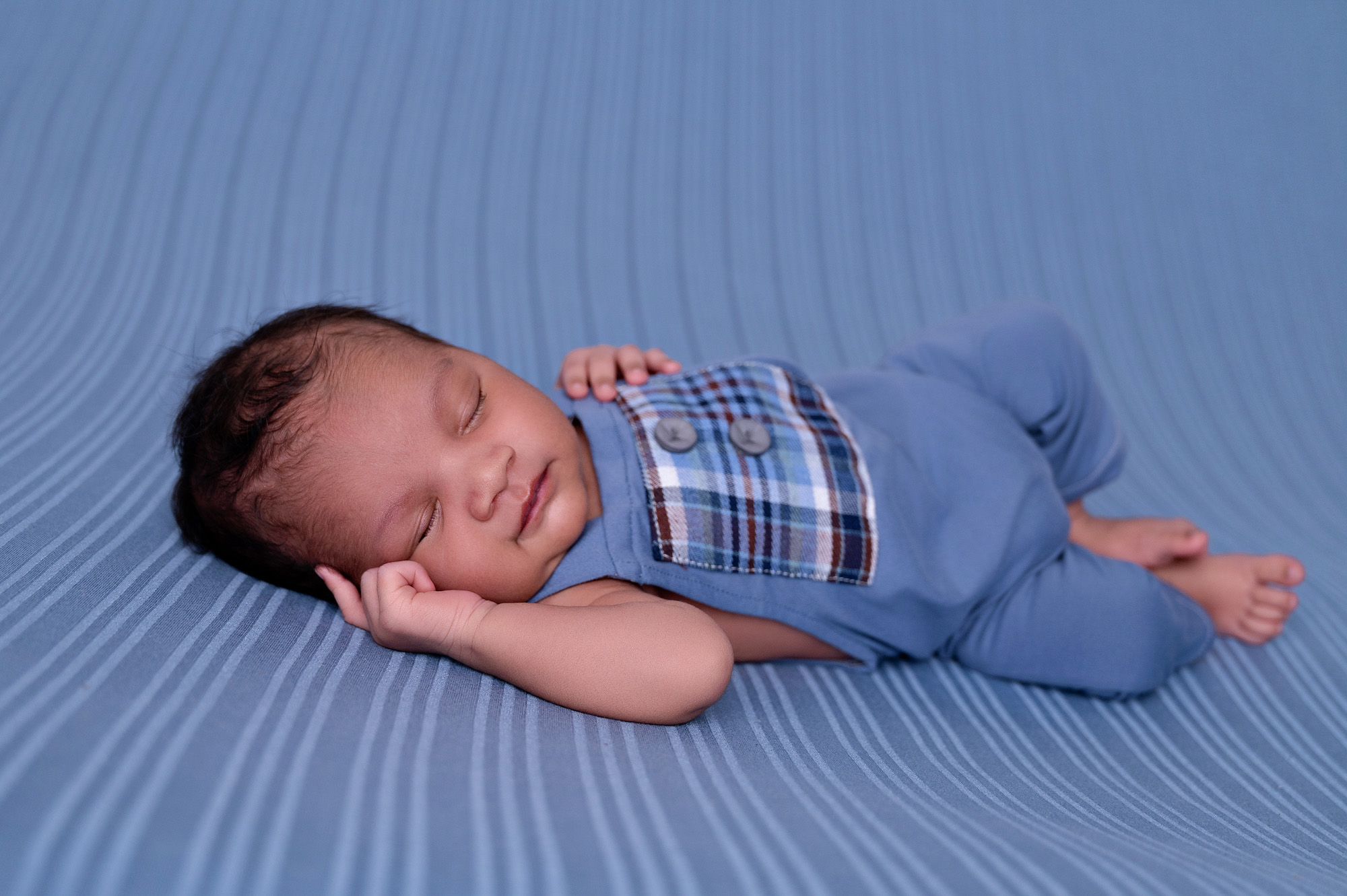 Newborn baby boy in a blue outfit sleeping on a blue backdrop — Pretoria newborn photography studio.