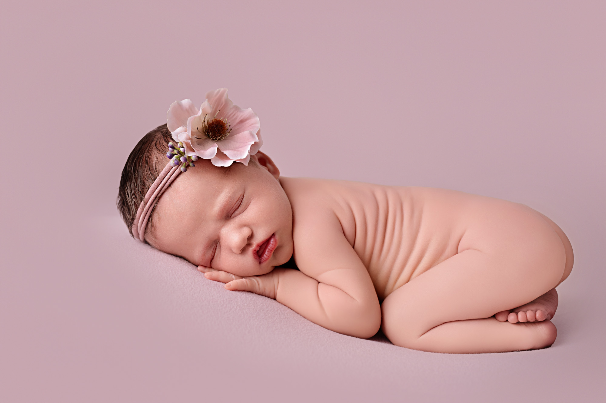 Pretoria newborn photographer studio portrait of a baby girl wrapped in nude tones on a soft pink backdrop.