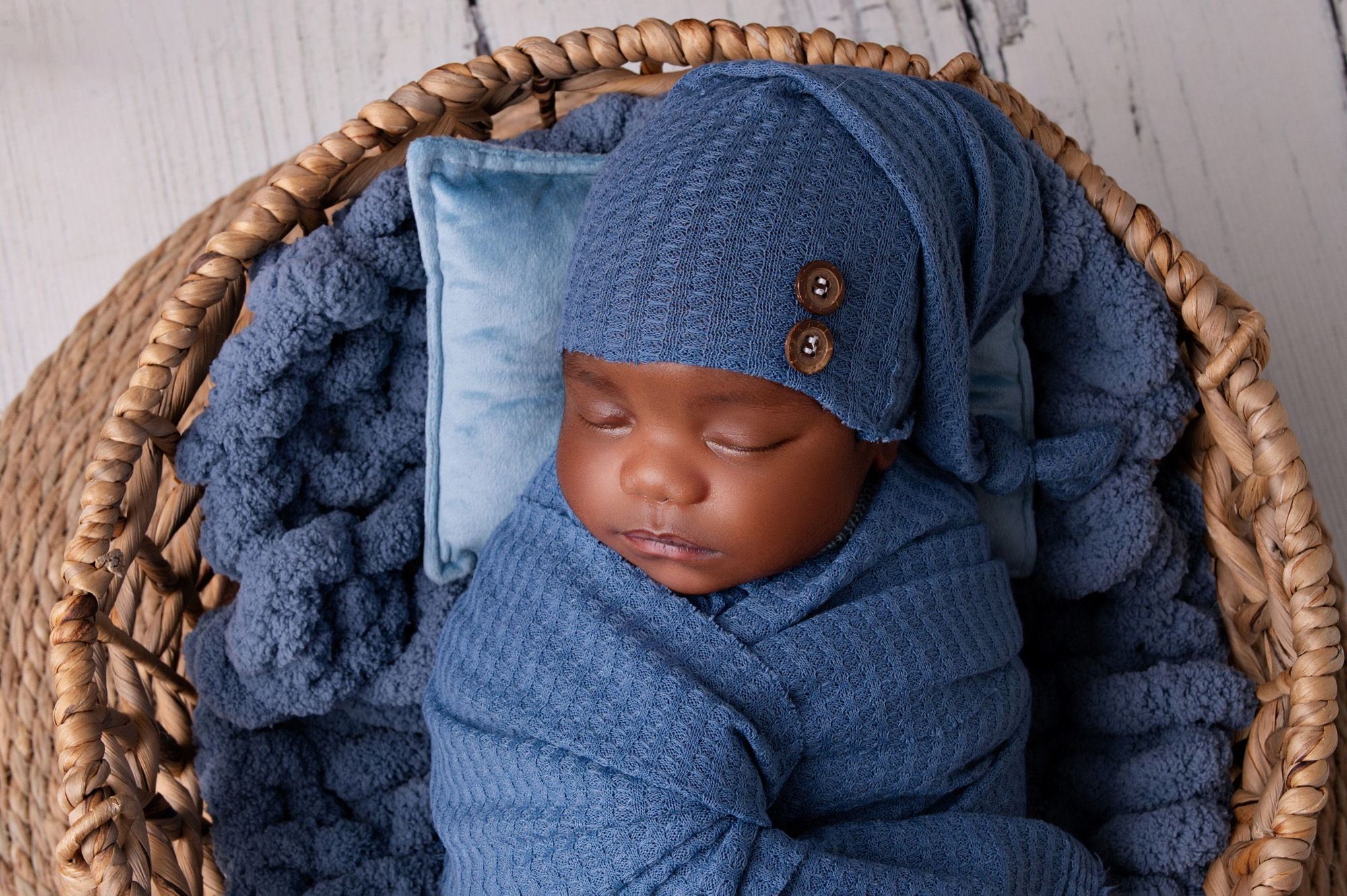 Newborn baby boy in a blue knitted outfit sleeping in a basket — Pretoria newborn photographer session.