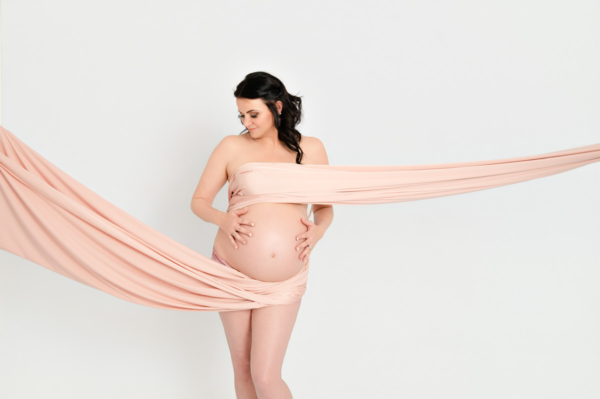 Fine-art maternity photoshoot with flowing peach fabric on white backdrop – maternity photographer Pretoria.