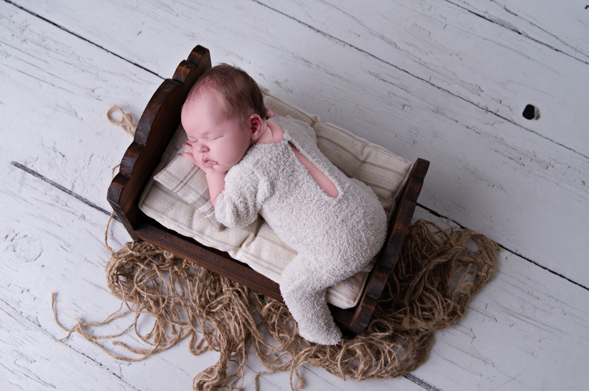 Newborn baby posed in a wooden bed with soft blankets — a calm moment during a stage when breastfeeding problems and struggling to latch are common.
