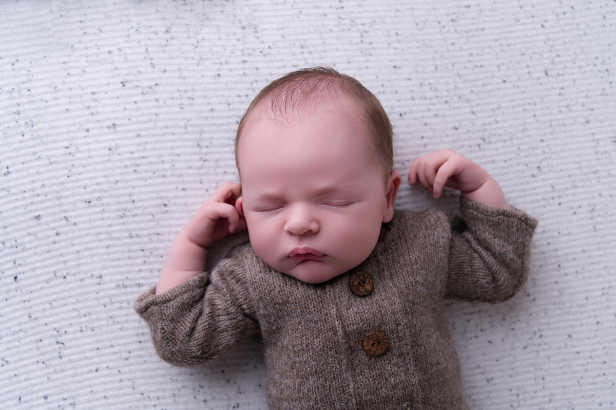 Newborn baby resting peacefully in a brown knitted romper — the early newborn stage when many parents face breastfeeding problems and struggling to latch.