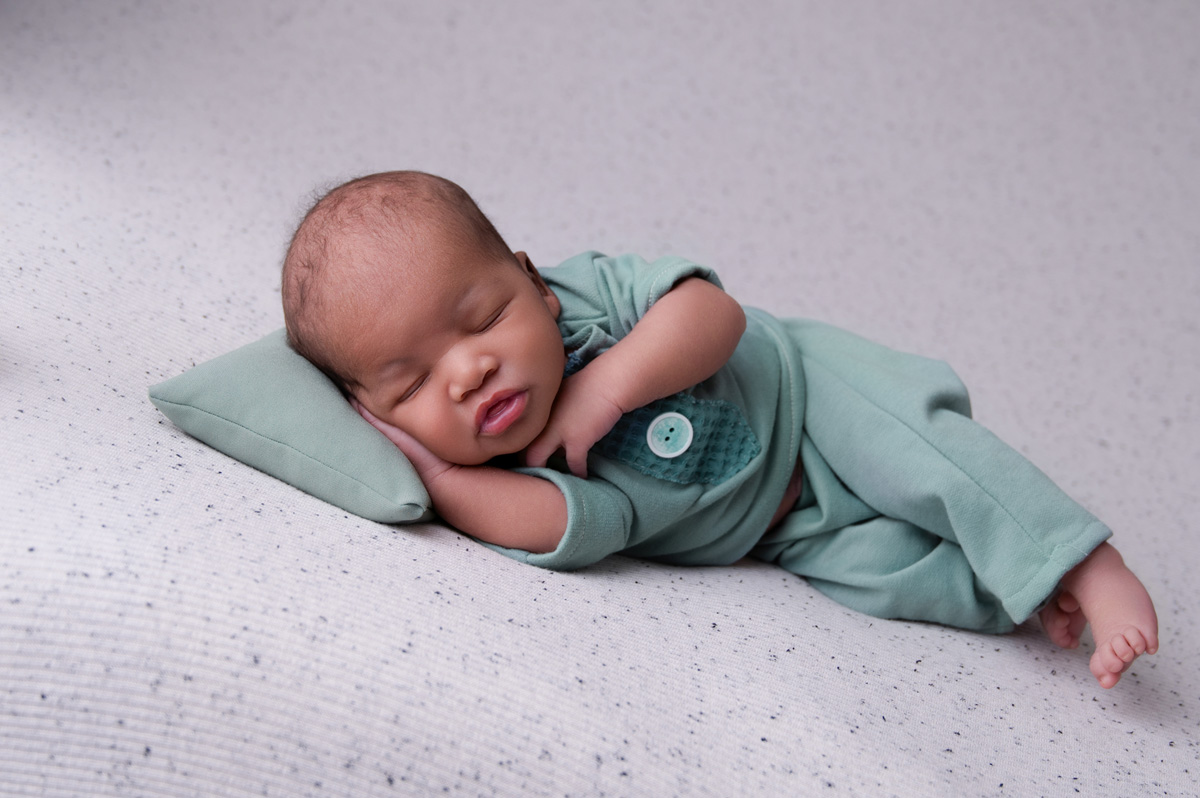Newborn baby boy in soft green outfit sleeping on white blanket – Pretoria newborn photographer.