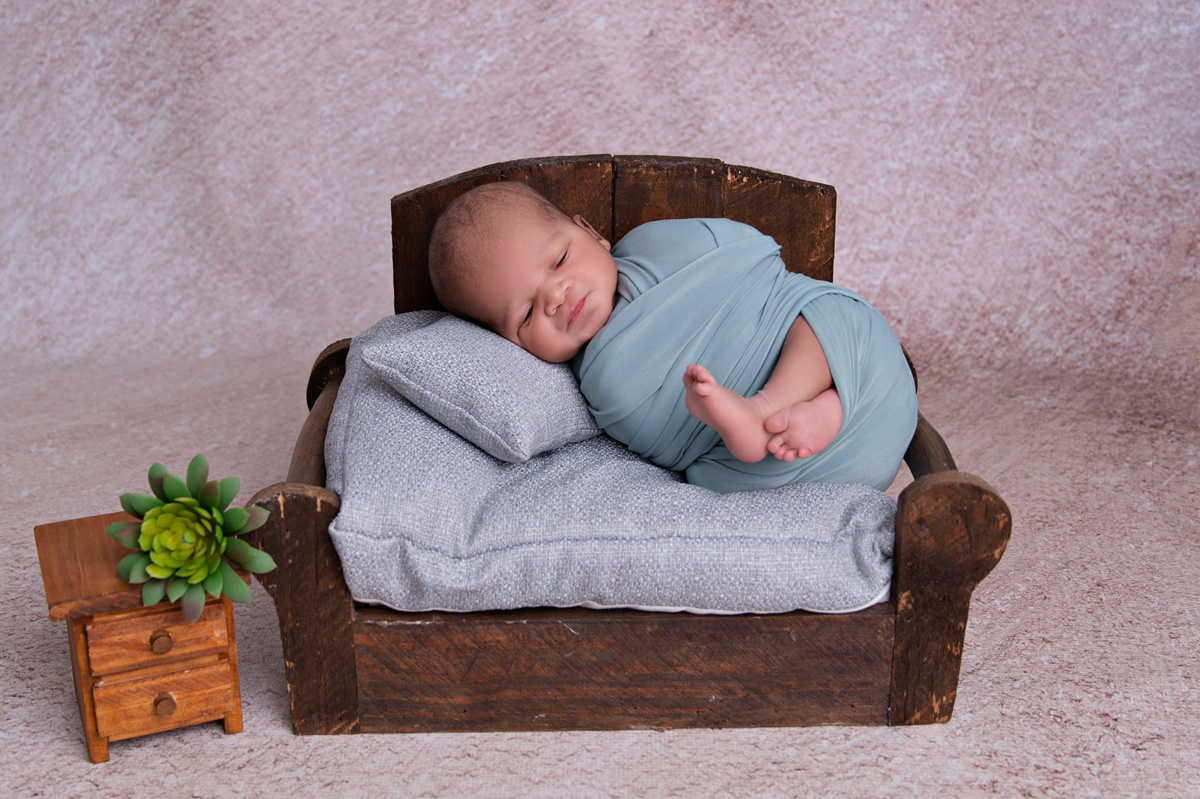 Sleeping newborn on mini wooden bed with grey pillows during studio session – newborn photoshoot Pretoria.