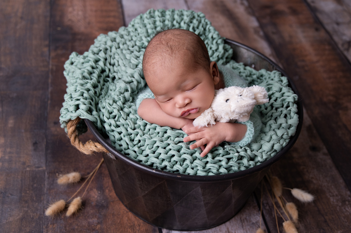 Newborn baby boy posed in wooden bucket with mint knitted blanket and teddy – newborn photoshoot Pretoria.