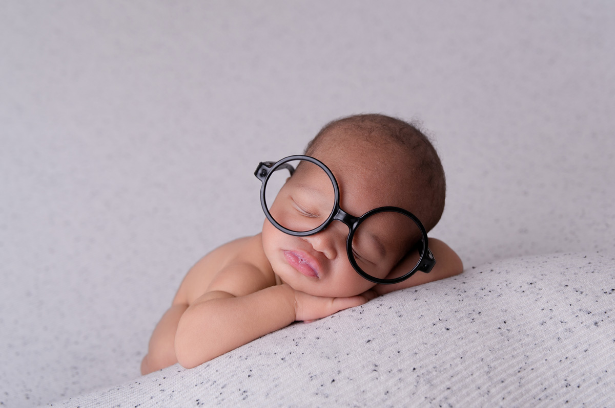 Cute newborn baby wearing round glasses on white blanket