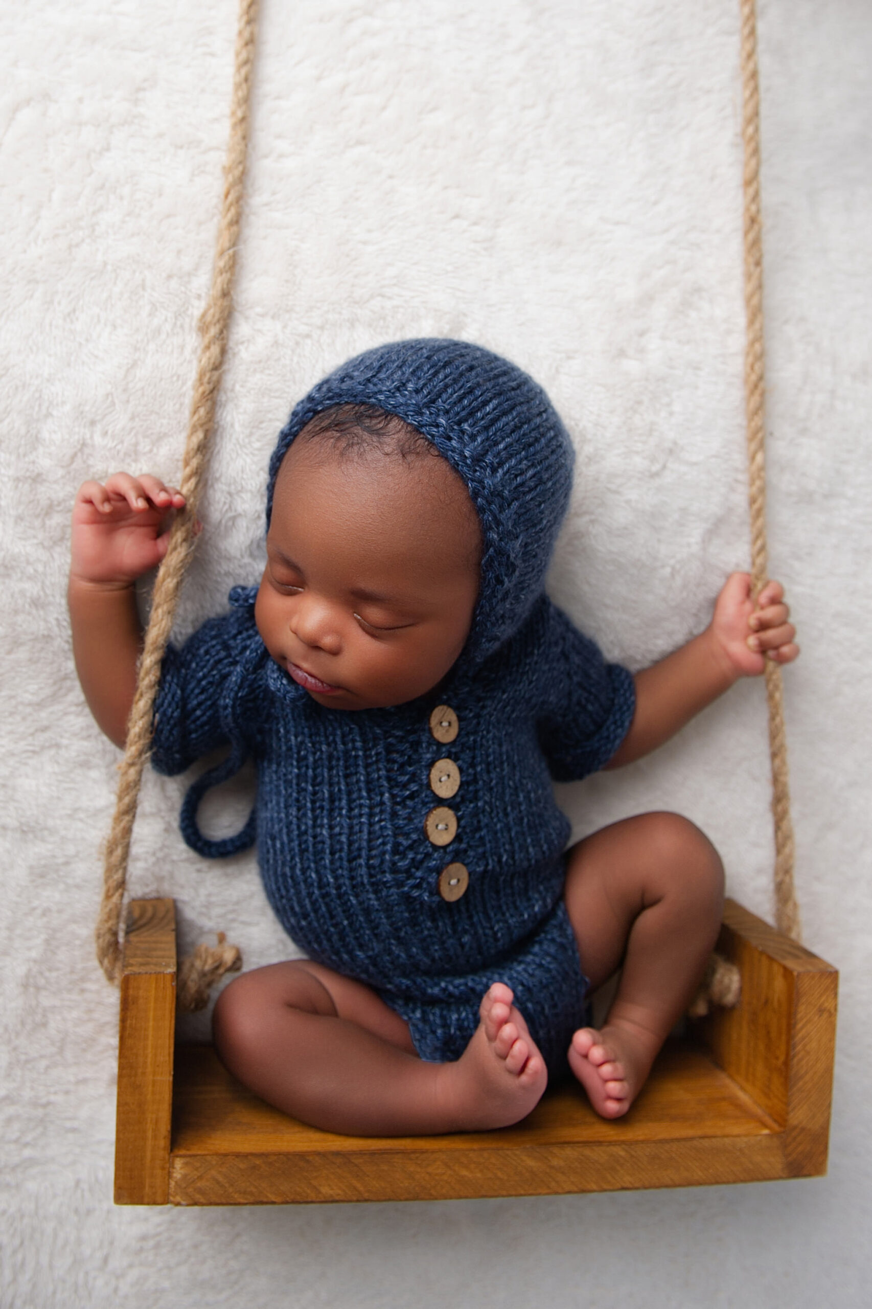 Newborn baby boy in blue knitted outfit posed in wooden bucket, reflecting the nurturing support families receive from Breastfeeding Clinics in the Moot.