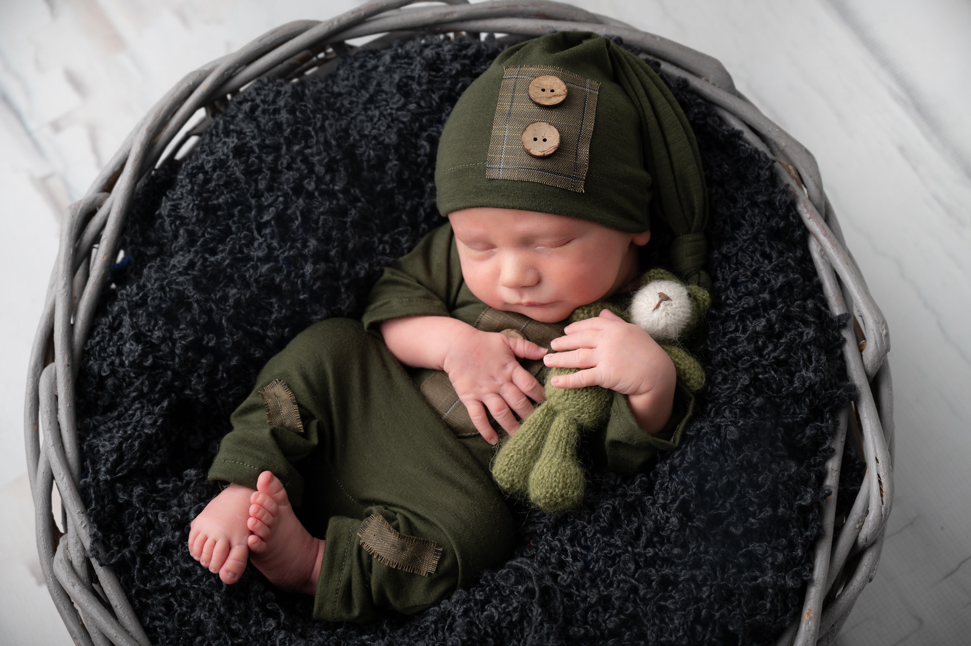 Newborn baby boy in green knitted outfit lying in black basket