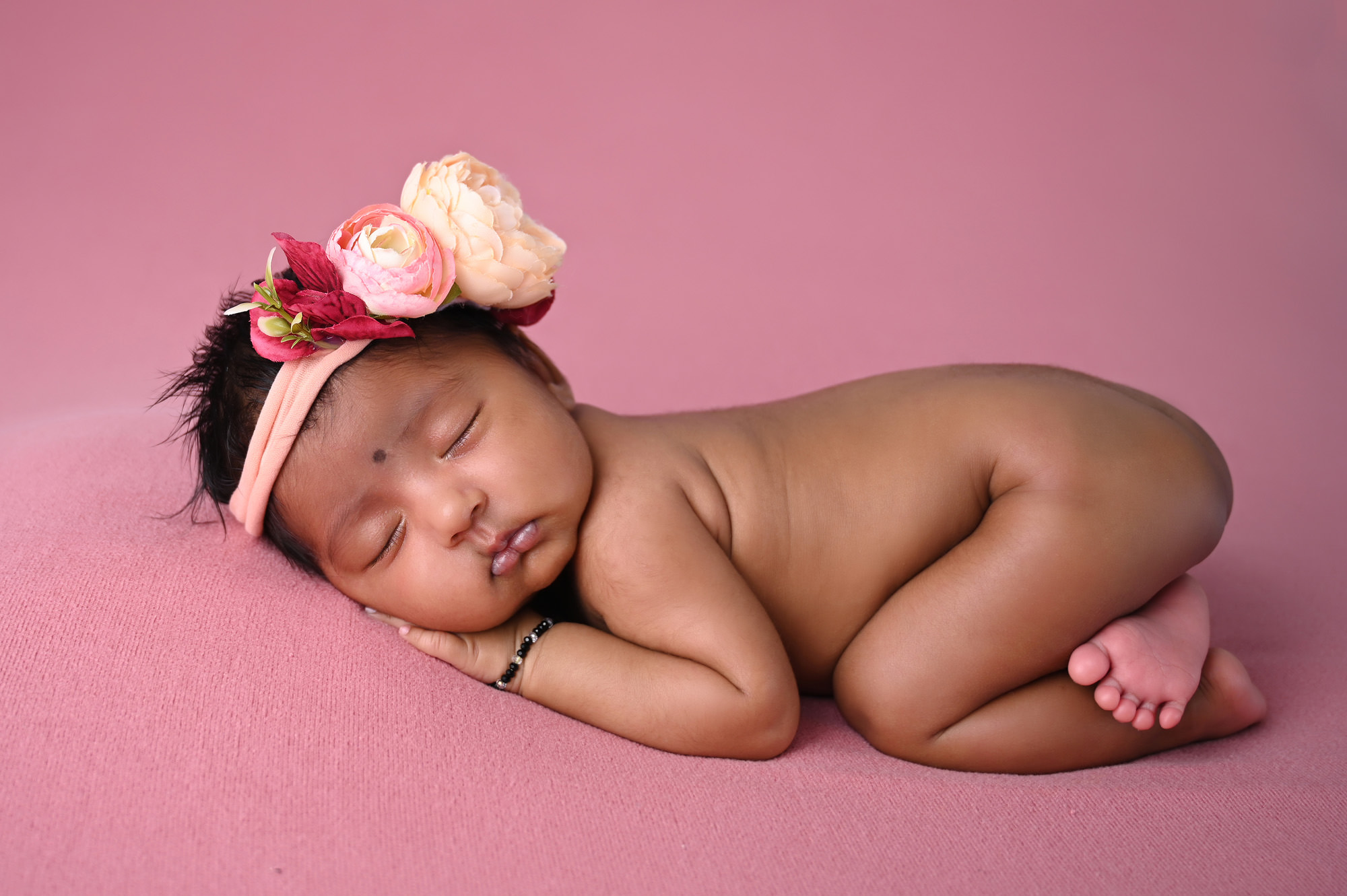 Newborn baby girl sleeping on soft pink backdrop with floral headband, capturing the peaceful newborn stage supported by Breastfeeding Clinics in the Moot.