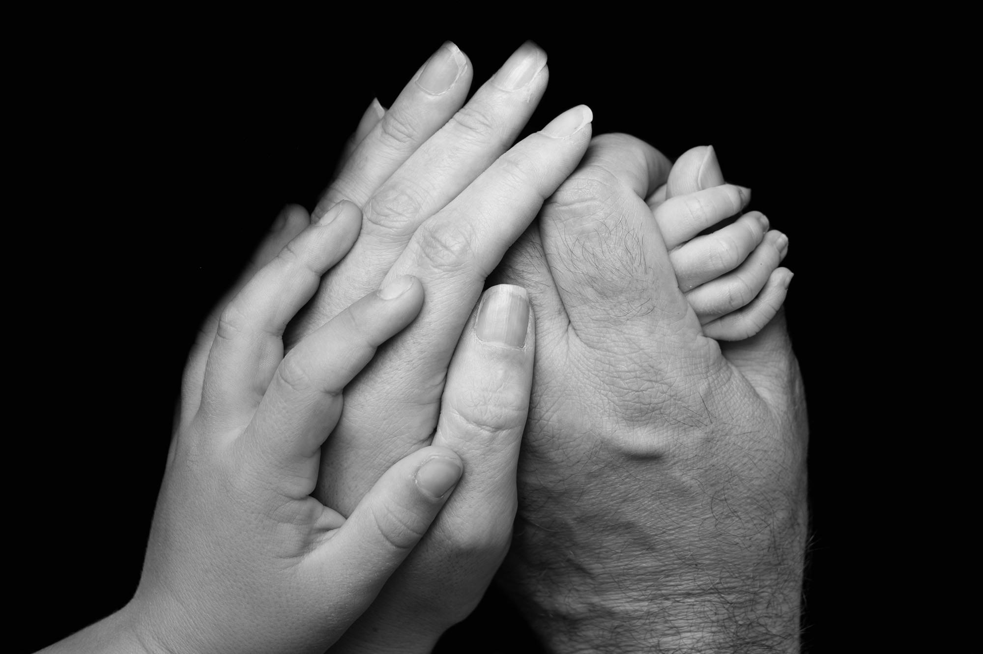Artistic black-and-white newborn feet held by parents’ hands, celebrating bonding