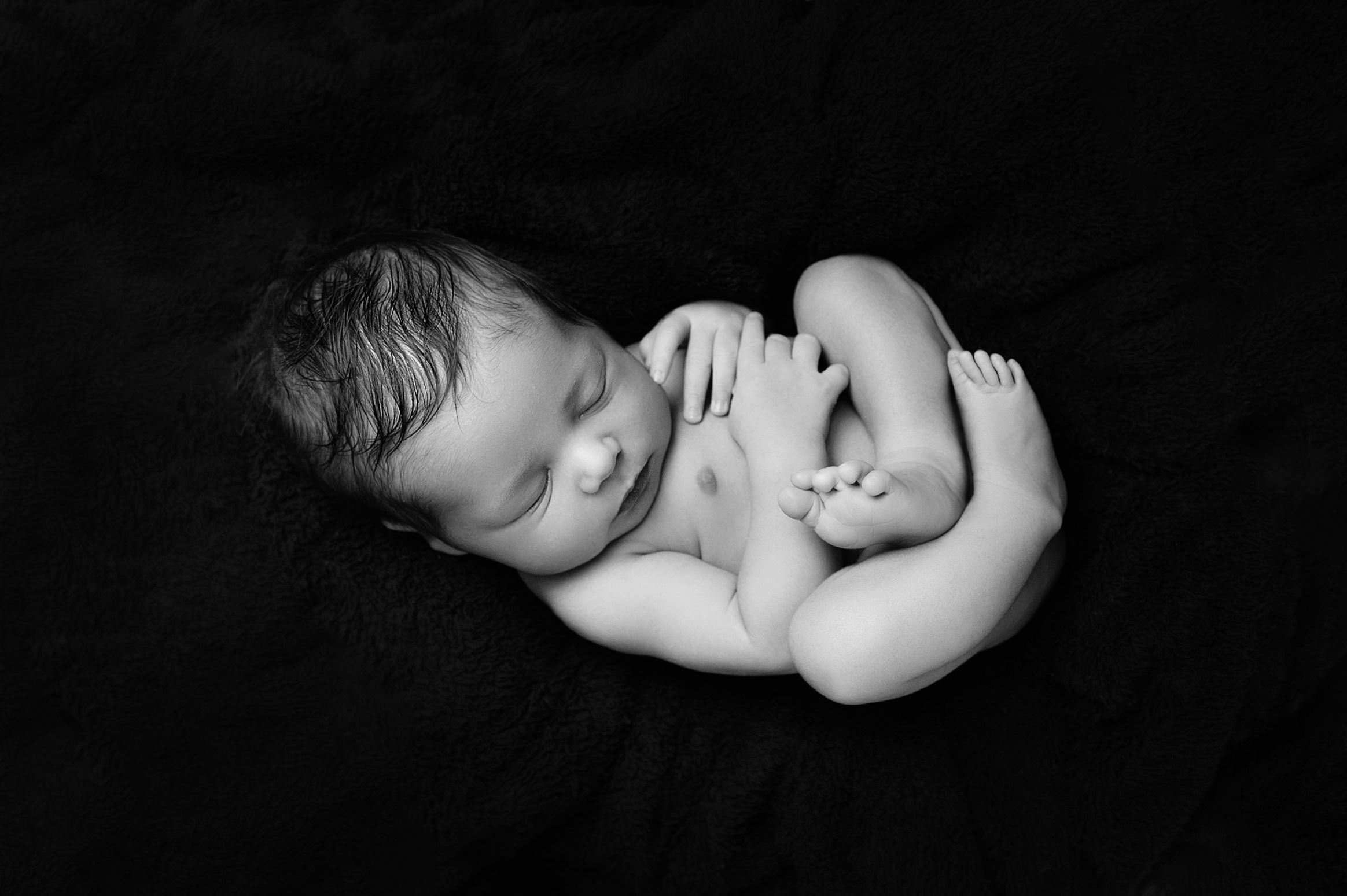 Newborn baby in curled pose on black blanket, part of early parenting and breastfeeding in PTA support journey.