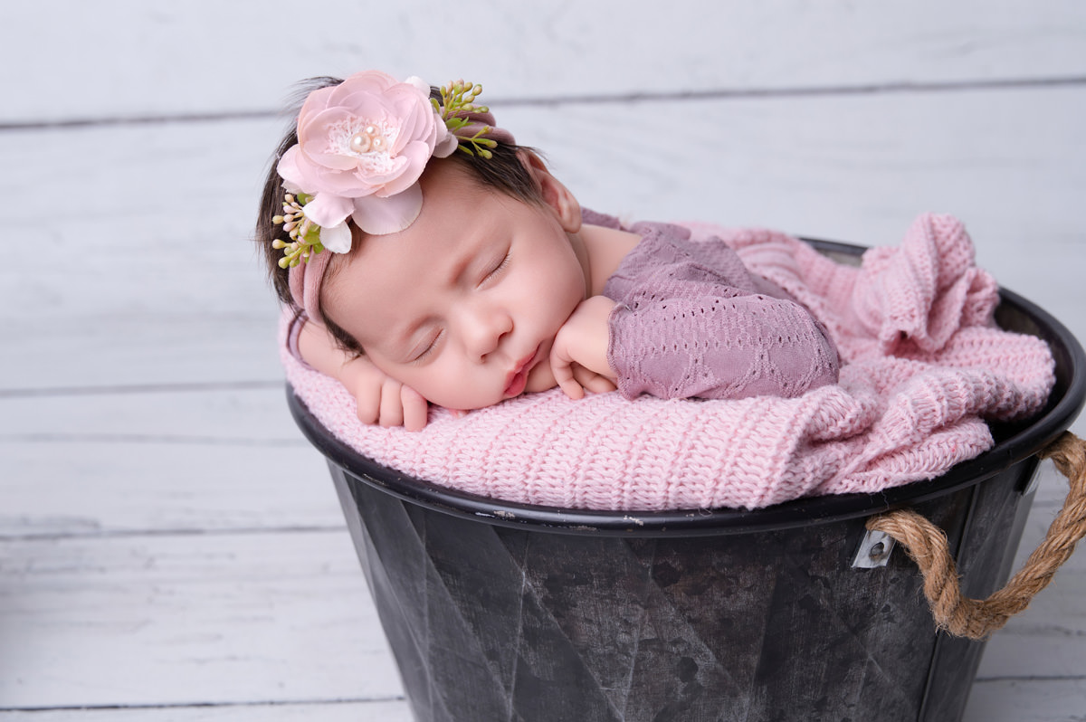 Newborn baby girl wrapped in soft pink sleeping in bucket prop,