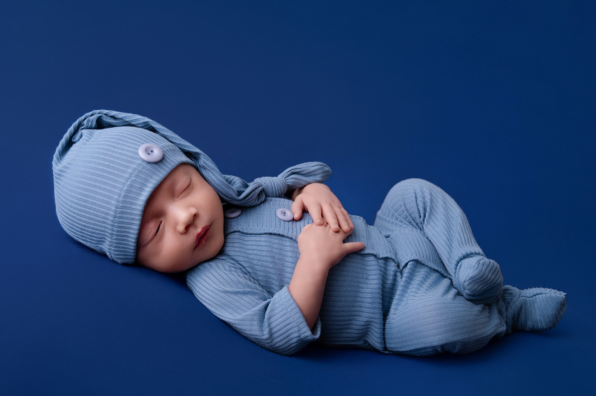 Pretoria newborn photographer capturing a baby boy in a blue outfit with a long knitted hat on a dark blue backdrop.