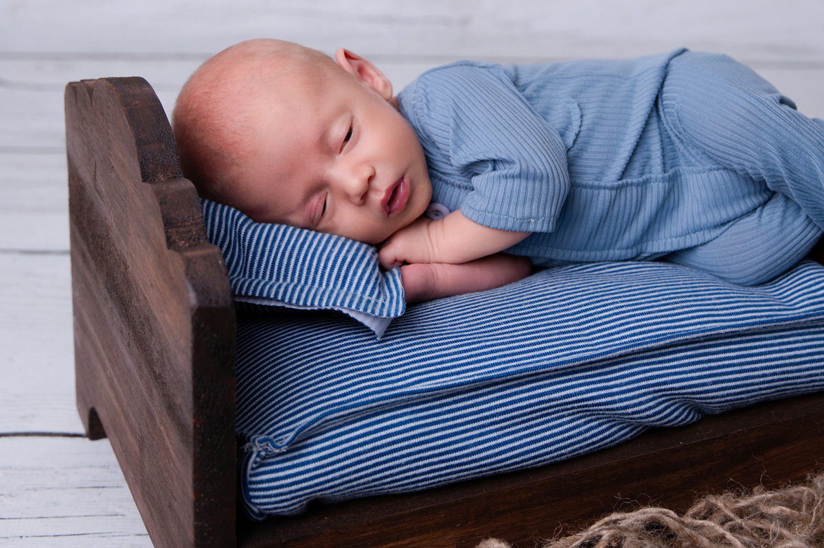 Newborn baby boy sleeping on a blue mattress in a wooden crate