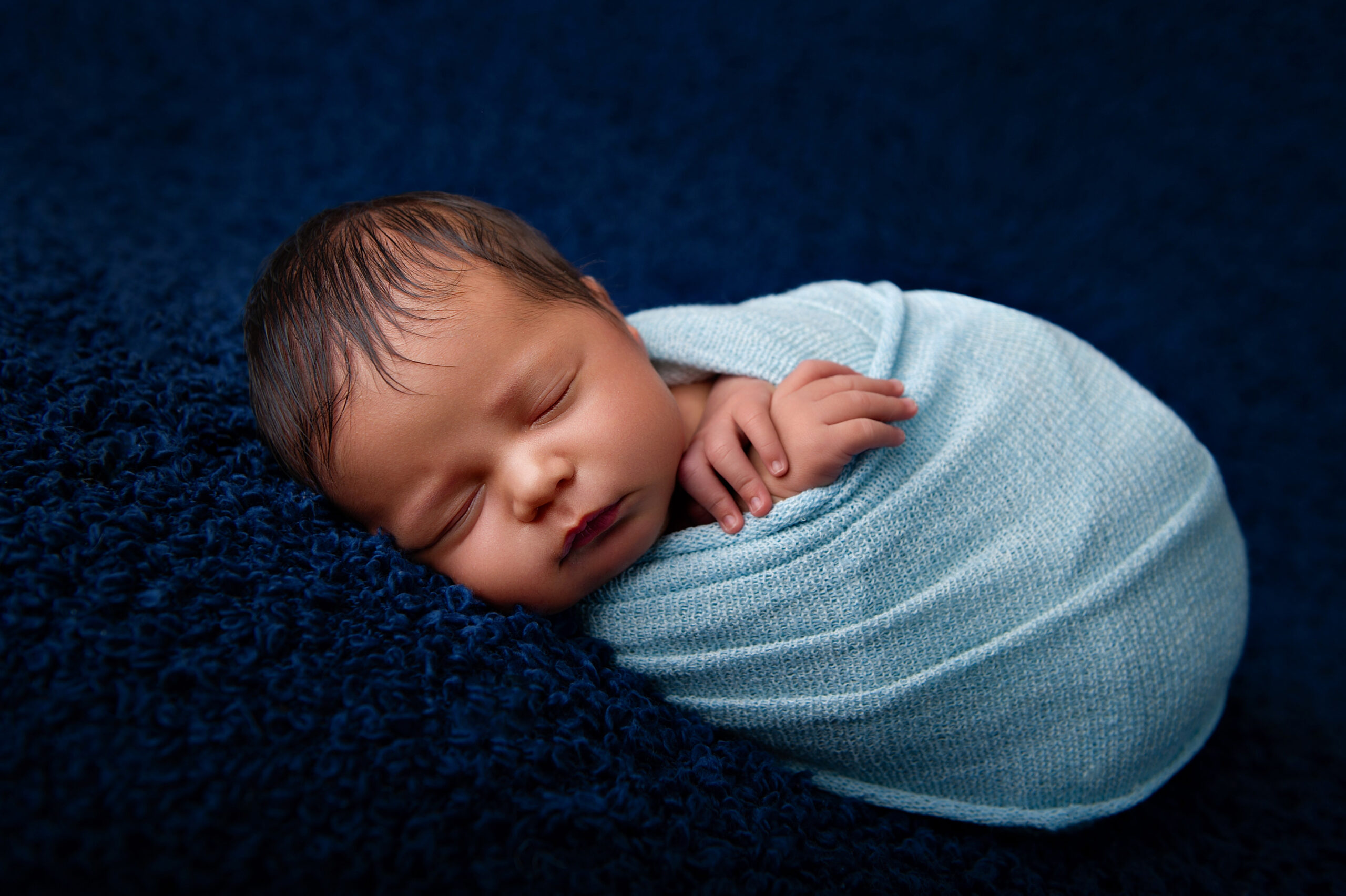 Newborn baby boy wrapped in light blue on dark blue backdrop,
