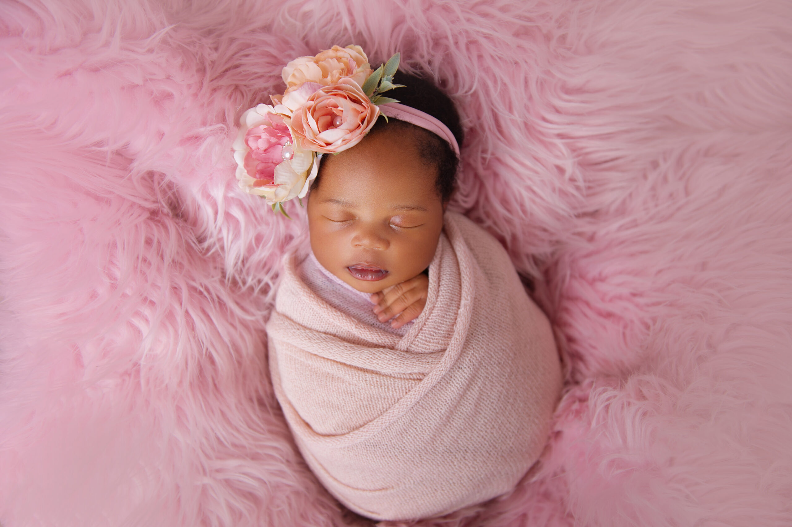 Newborn baby girl wrapped in soft pink with floral headband