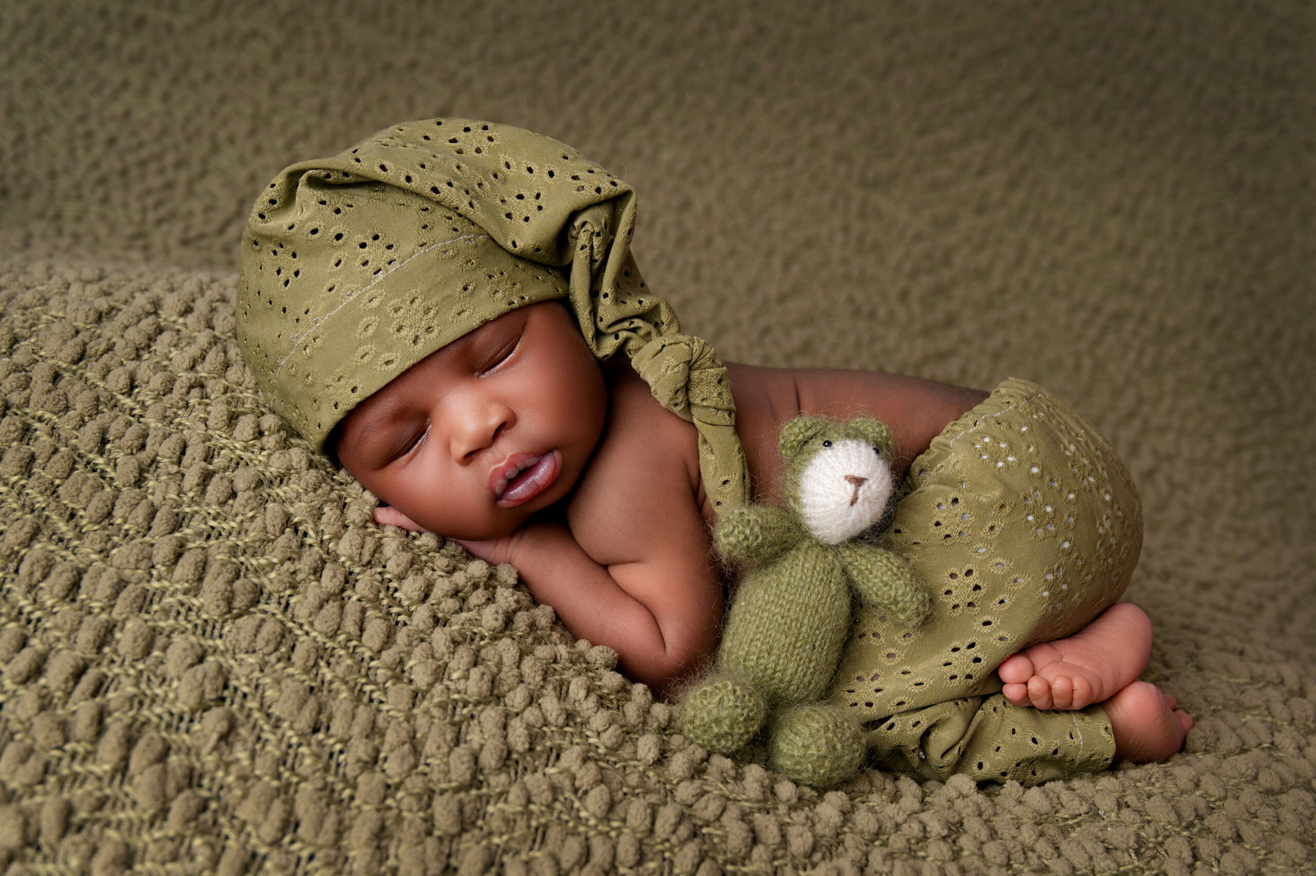 Sleeping newborn baby in green knitted outfit with teddy
