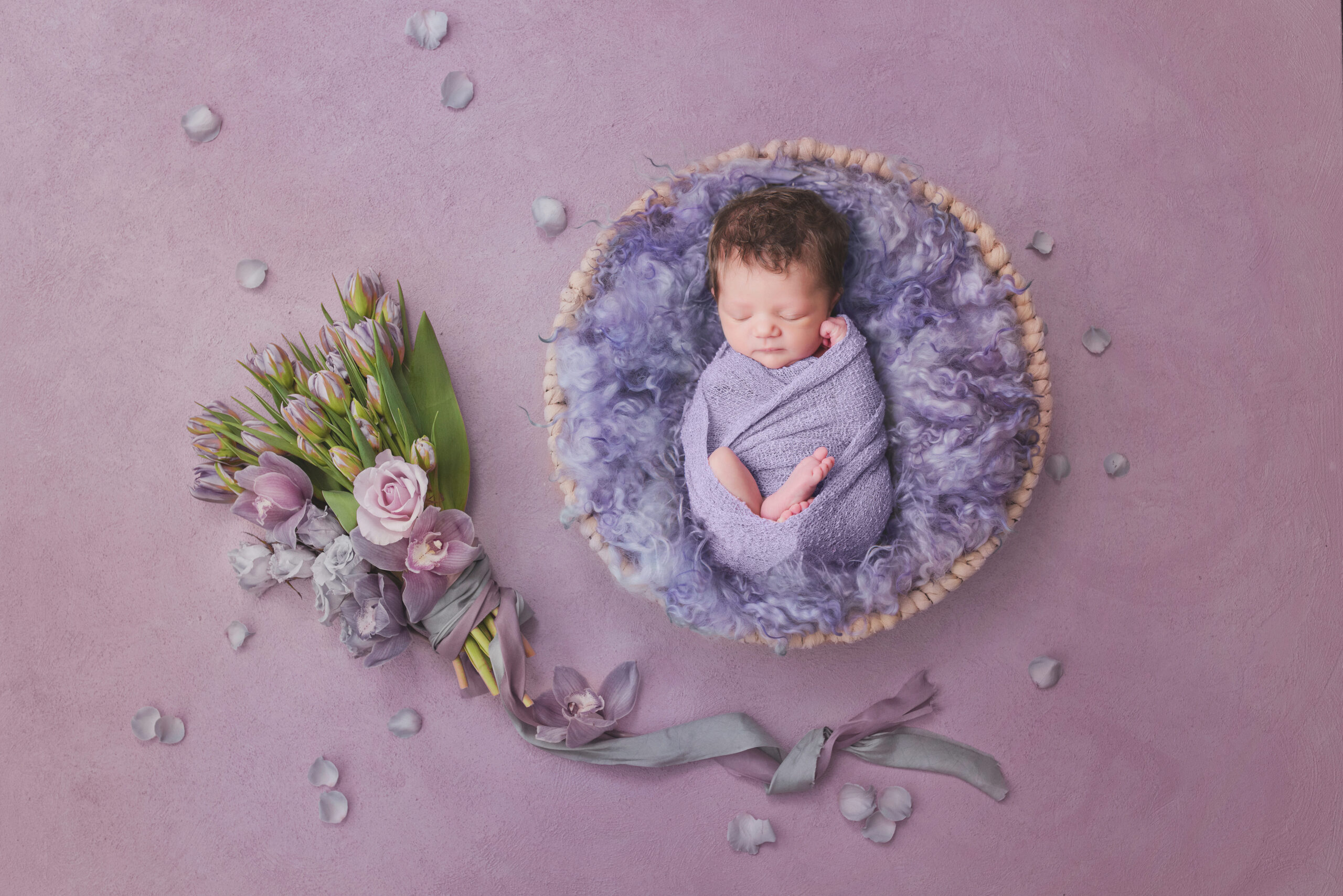 Newborn baby girl wrapped in lilac inside textured basket, representing early newborn care guided by a lactation consultant.