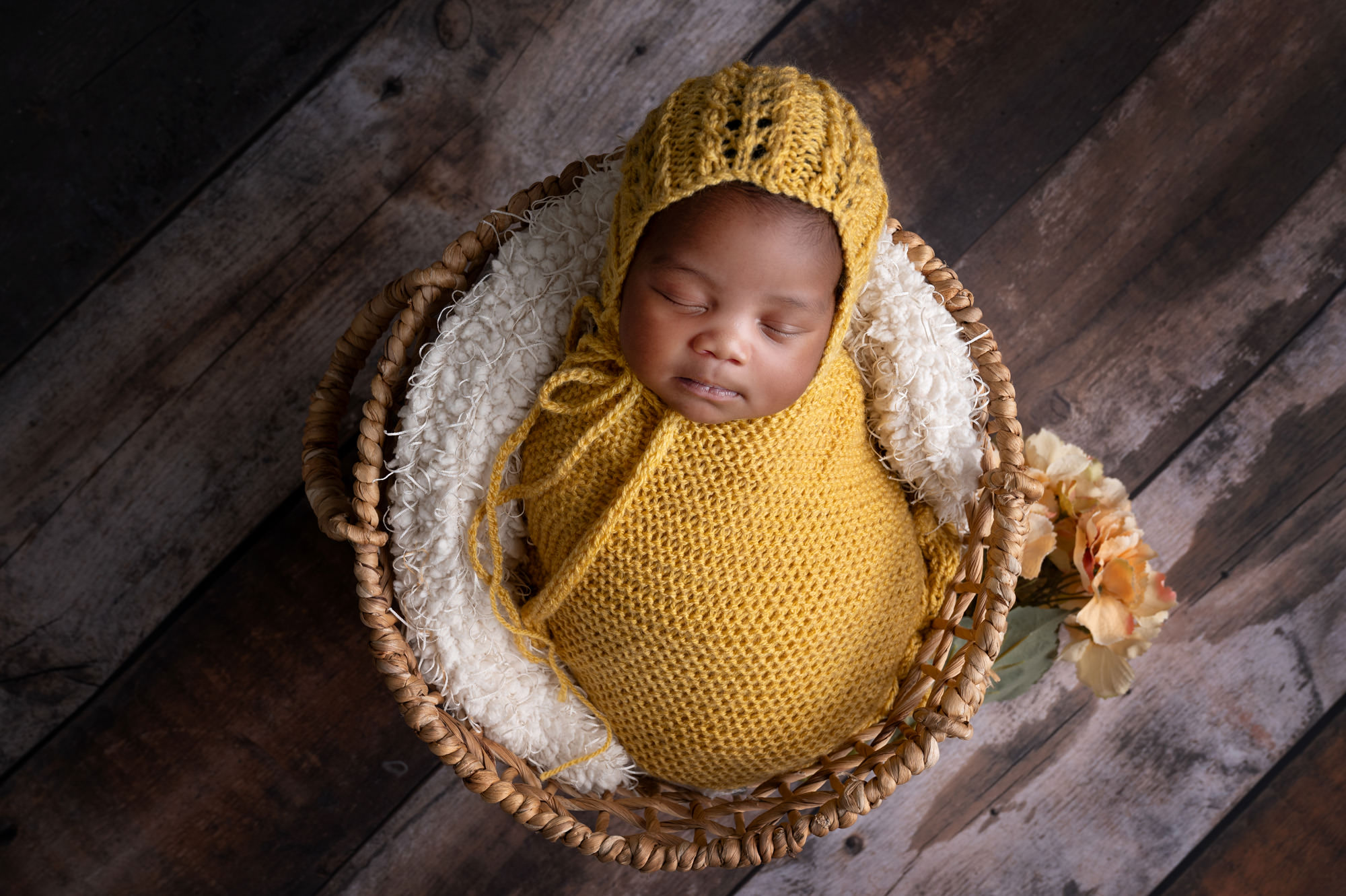 Sleeping newborn wrapped in mustard yellow inside woven basket,