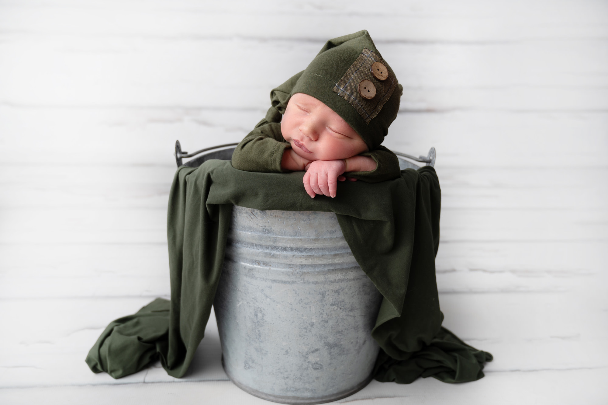 Newborn baby boy posed in green outfit over bucket prop
