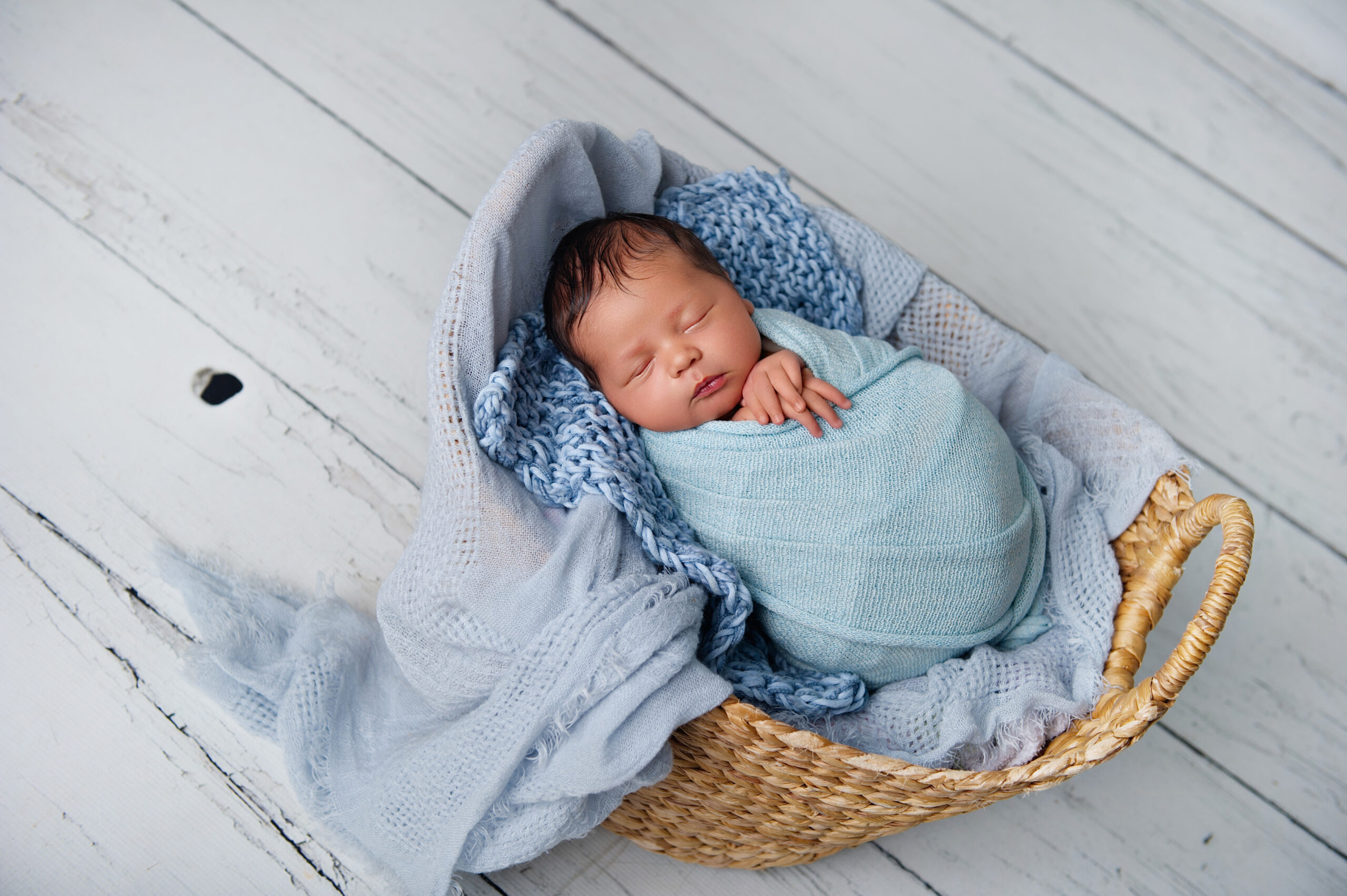Newborn baby boy wrapped in soft blue inside wicker basket, capturing peaceful newborn routines supported by a lactation consultant.