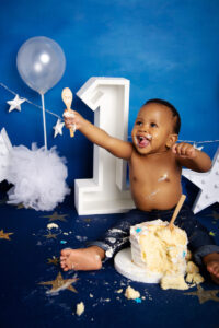 Excited baby pointing beside number one backdrop during cake smash session