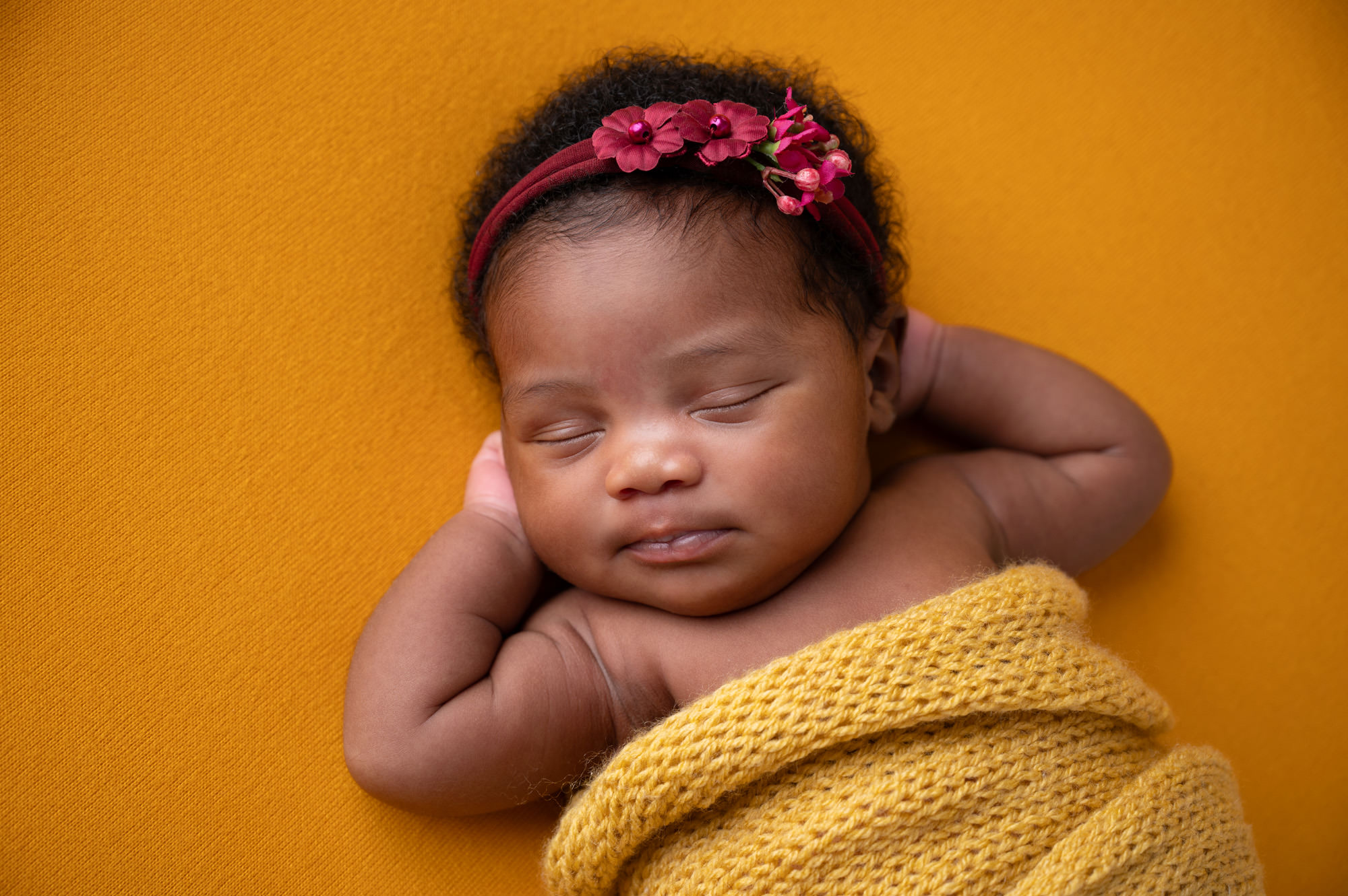 Newborn baby girl sleeping on mustard yellow blanket with floral headband,