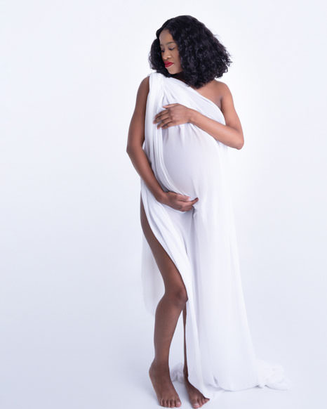 Elegant maternity portrait of pregnant woman in white gown, representing relaxation and care offered by Pregnancy Massage Therapists in Pretoria East.