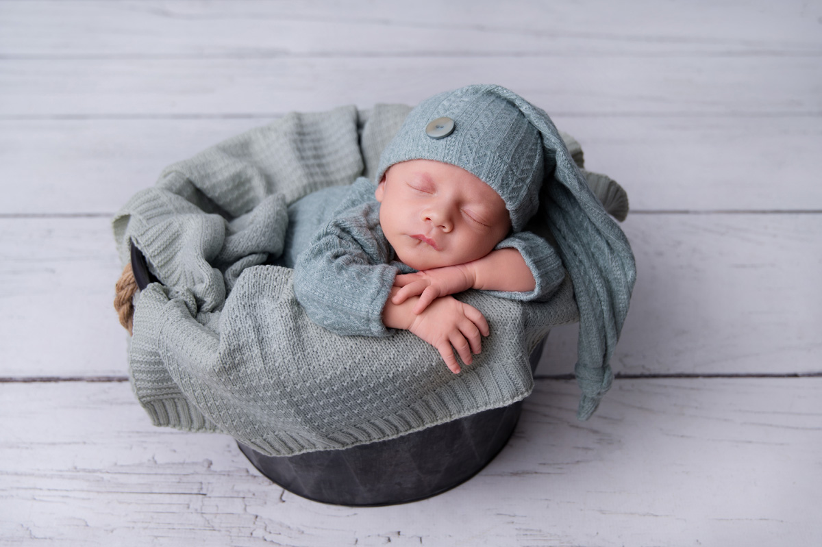 Sleeping newborn baby boy wrapped in soft green knit in studio setup, reflecting calm recovery and support from Pregnancy Physiotherapists in Montana.