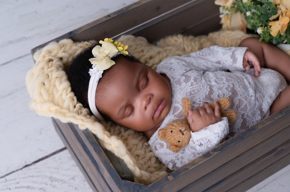 Pretoria newborn photographer session with a baby girl posed in a grey crate with cream fur and a floral headband.