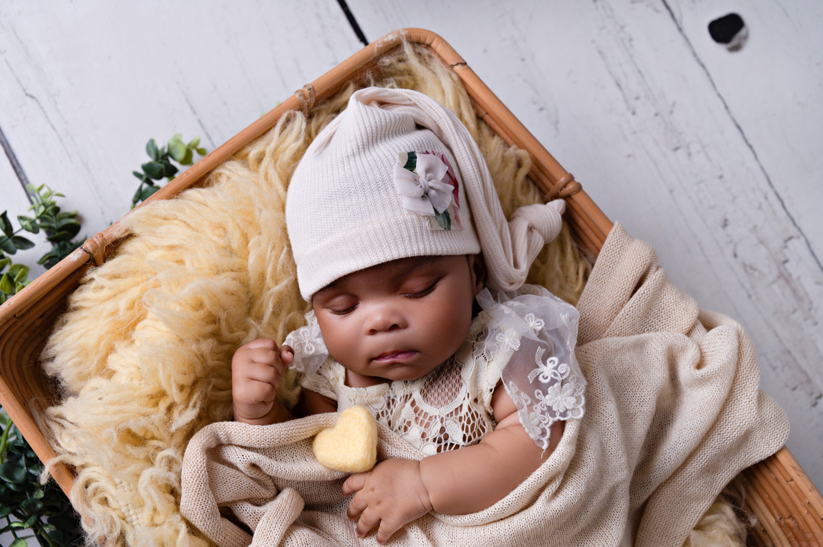 Newborn baby girl in a cream outfit and bonnet holding a tiny teddy — newborn photography Pretoria.