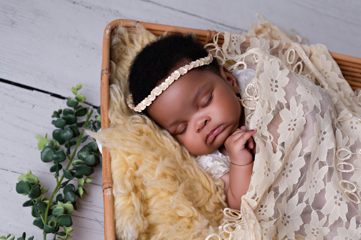 Pretoria newborn photographer capturing a baby girl wrapped in lace, posed in a wooden box with yellow fur.