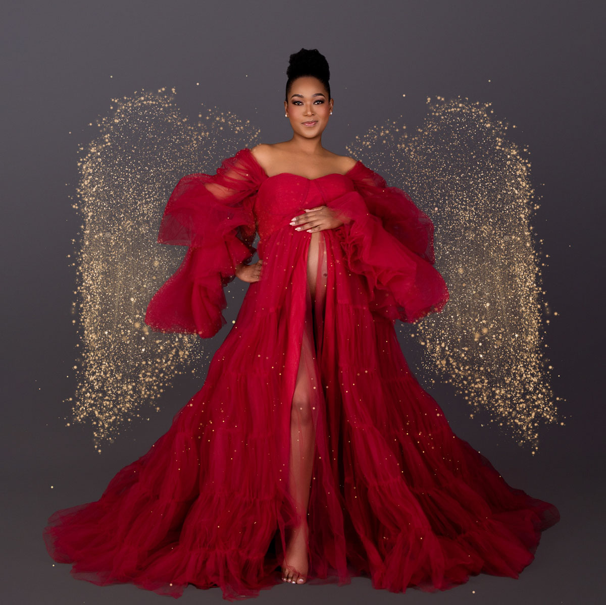 Expecting mother in a flowing red dress standing in front of a golden wing-style backdrop, symbolising strength and nurturing often associated with La Leche League support.