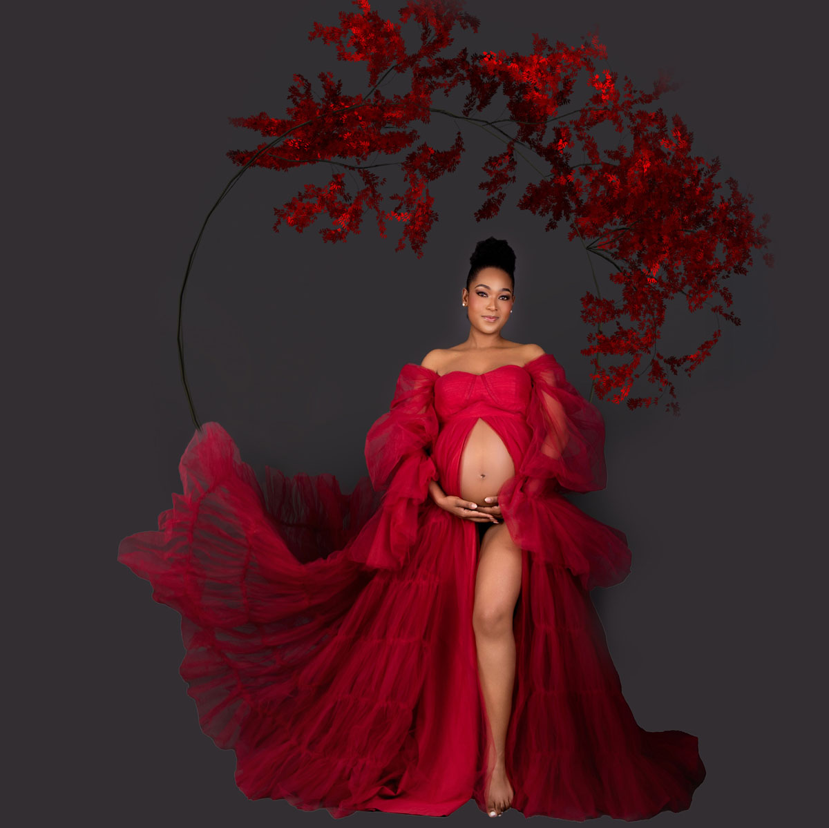Studio maternity portrait of an expecting mother in a red gown with a red floral arc,