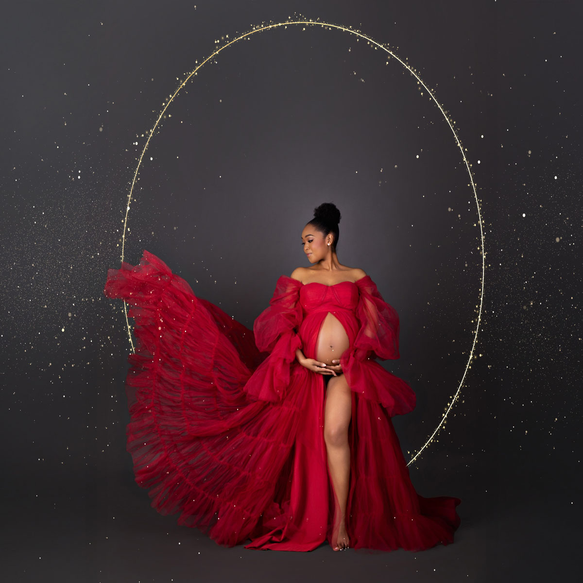 Pregnant woman in a flowing red maternity gown posing in studio with a gold circular backdrop, styled for a calm, elegant look often celebrated by La Leche League supporters.